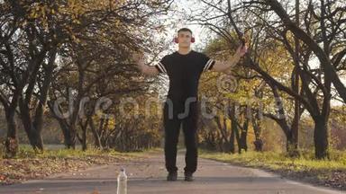 日落时分，一位戴着耳机和黑色运动服的高加索青年运动员在秋天公园跳绳的肖像